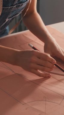 Bir kadın pembe kumaş parçasına şablon çiziyor. Çizgilerin düz olduğundan emin olmak için bir cetvel ve kalem kullanıyor. Ayrıntılara hassasiyet ve dikkat kavramı