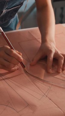 Bir kadın bir kağıt parçasına şablon çiziyor. Kalem ve cetvel kullanıyor.