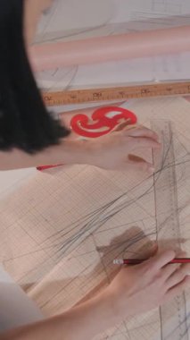 Bir kadın bir kağıt parçasına tasarım çiziyor. Tasarımı kesmek için bir cetvel ve makas kullanıyor.