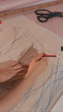 Bir kadın bir kağıt parçasına elbise çiziyor. Bir cetvel ve kalem kullanıyor.