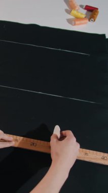 Bir kadın bir kumaş parçasını cetvelle ölçüyor. Kumaşı işaretlemek için tebeşir kullanıyor.