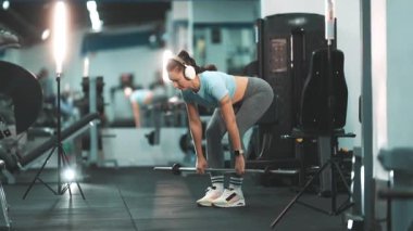 Kulaklıklı atletik kadın modern bir spor salonunda ağırlık kaldırma egzersizi yapıyor.