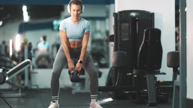 Spor salonundaki antrenman sırasında kulaklık takan, ağırlık kaldıran odaklanmış bir kadın.