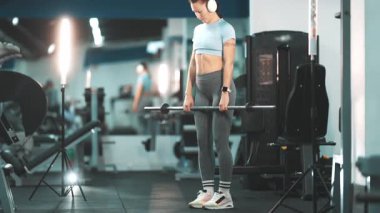 Romen kaldırma egzersizi yapan güçlü formda bir kadın sırt ve bacak kasları için halter kullanıyor.