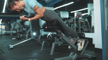 Kadın sporcu, spor salonunda bel kaslarını aşırı uzatma makinesiyle güçlendiriyor.