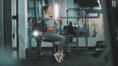 Spor kıyafetleri içinde beyaz bir kadın spor salonunda göğüs kaslarını sinek makinesiyle çalıştırıyor.