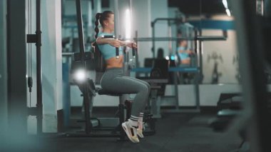 Spor salonundaki kelebek makinesinde göğüs sineği egzersizi yapan zinde genç bir kadın.