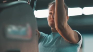 Spor salonundaki egzersiz makinesinde barfiks çekerek kas ve güç kazanan atletik bir kadın.