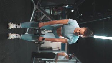 Güçlü kasları olan sağlıklı genç bir kadın spor salonunda kollarını ve sırtını kollarıyla eğitiyor.