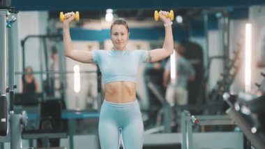 Odaklanmış atletik kadın modern bir spor salonunda dambıl omuz çalışması yapıyor.