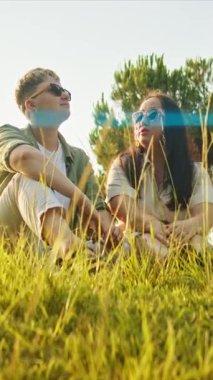 Parkta çimlerde oturan şık çift yaz gününün tadını çıkarıyor.