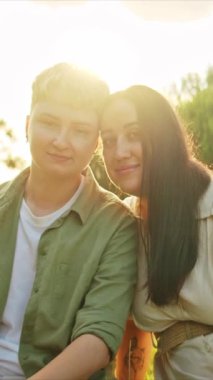 Romantik lezbiyen çift çimenlerde oturmuş doğada günbatımının tadını çıkarıyor.