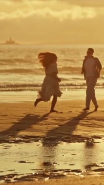 Romantik çift, altın bir günbatımında sahilde neşeli bir koşu yapıyor.