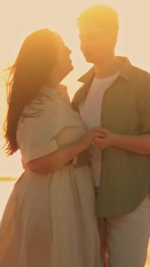 Güzel altın bir gün batımında kumlu bir sahilde el ele tutuşup kucaklaşan sevgi dolu bir çift.