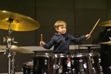 Ses geçirmez müzik okulu stüdyosunda sopalarla davul çalan genç bir çocuk.