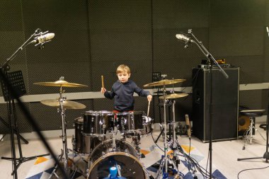 Genç bir çocuk bateri çalıyor, modern bir kayıt stüdyosunda müzik yeteneği geliştiriyor.