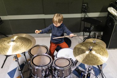 Genç çocuk davul çalıyor, ritmi öğreniyor ve ses geçirmez bir odada yaratıcılığını ifade ediyor.