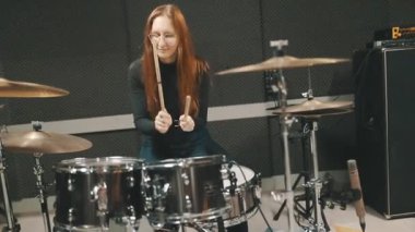 Ses geçirmez bir odada prova yaparken davul çalan kızıl saçlı tutkulu bir bayan müzisyen.