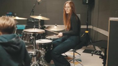 Müzik stüdyosundaki bir derste davul setinde çalışan kızıl saçlı bir baterist.