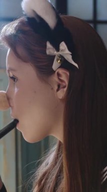 Kostümlü makyaj yapan genç bir kadın fırçanın sapını dişleriyle sıkıyor. Orta çekim