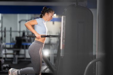 Modern fitness merkezinde üst vücut kaslarını çalıştıran genç bir kadın.