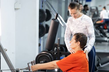 Modern bir spor salonunda kürek çeken bir kadına kişisel antrenör rehberlik ediyor.
