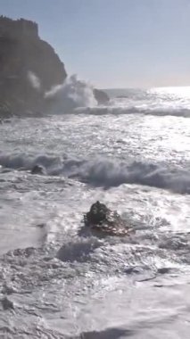 Deniz dalgaları kayalara çarpar ve kıyıları ağır çekimde kaplar. Orta çekim