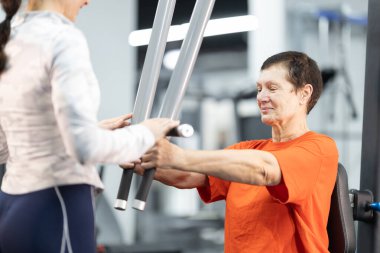 Üst düzey kadın, kadın kişisel antrenörünün yardımıyla göğüs presi egzersizi yapıyor.