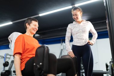 Tecrübeli koç, modern fitness merkezinde yaşlı bir kadının sağlıklı yaşam tarzını sürdürmesine yardım ediyor.