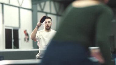 Beyazlı bir adam spor salonunda pinpon oynarken konsantre oluyor.