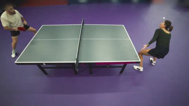 Erkek ve kadın, mor zemini olan bir spor kulübünde masa tenisi oynuyorlar.