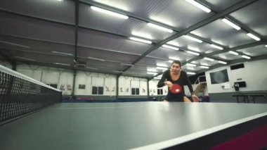 Profesyonel masa tenisi oyuncusu yoğun bir maç sırasında topa kürekle vuruyor.