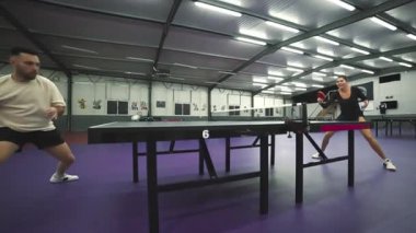 Genç bir adam ve bir kadın spor salonunda pinpon oynuyorlar.