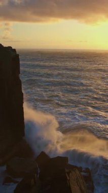 Gün batımında deniz dalgaları kayalık bir uçuruma çarpar. Orta çekim