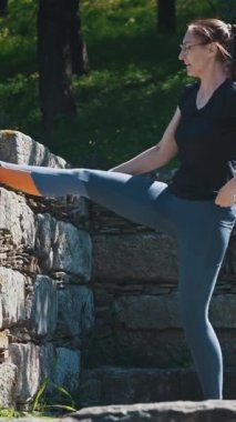 Atletik kadın ayağını taş bir duvara atarak esneme hareketleri yapıyor. Orta çekim