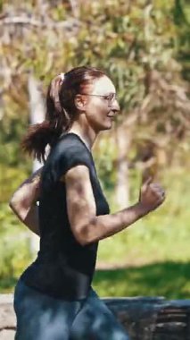 Yeşil parkta koşan gözlüklü, yetişkin, sportif bir kadın. Orta çekim