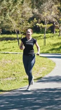 Yeşil parkta koşan gözlüklü, gülümseyen sporcu kadın. Orta çekim