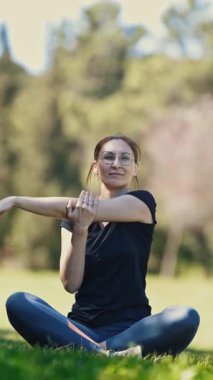 Gözlüklü gülümseyen yetişkin kadın lotus pozisyonunda oturur ve kollarını uzatır. Orta çekim