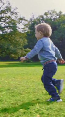 Küçük bir çocuk annesinin kollarına koşar ve onu çimlerin üzerine atar. Orta çekim