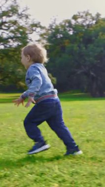 Küçük bir çocuk parkta koşar ve annesinin kollarına düşer. Orta çekim