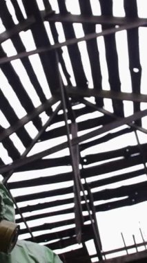 Koruyucu takım elbiseli ve gaz maskeli bir adam kameraya doğru eğiliyor ve tuhaf bir şekilde bakıyor. Orta çekim