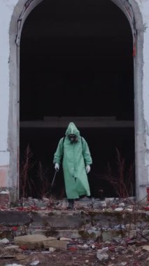 Gaz maskeli ve koruyucu giysili bir adam dağınık alanda yürüyor. Orta çekim