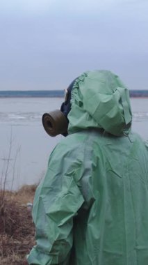 Kıyameti andıran bir kavram. Gaz maskeli, koruyucu takım elbiseli bir adam bulutlu manzaranın arka planına bakıyor. Orta çekim