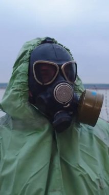Gaz maskeli bir adam koruyucu elbiseler giyip bulutlu manzaranın arka planına bakıyor. Orta çekim