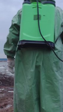 Gaz maskeli, koruyucu takım elbiseli bulutlu bir arazide yürüyen bir adam. Orta çekim