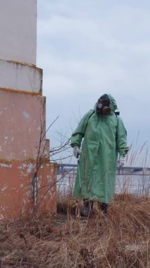Kıyamet sonrası konsepti: Gaz maskeli, koruyucu takım elbiseli bir adam terk edilmiş bir binanın etrafında dolaşıyor. Orta çekim