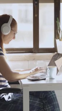 Genç bir kadın kahvaltıda kulaklıklı bir bilgisayarın başında çalışıyor. Orta çekim