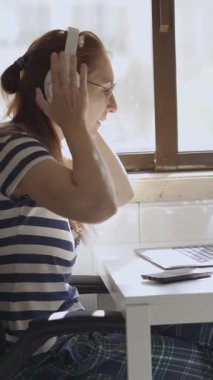 Genç bir bayan tasarımcı kulaklık takar ve dizüstü bilgisayarla çalışmaya başlar. Orta çekim