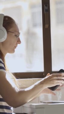 Kahvaltı masasında cep telefonu, dizüstü bilgisayarı ve kahvesi olan genç bir kadın. Orta çekim