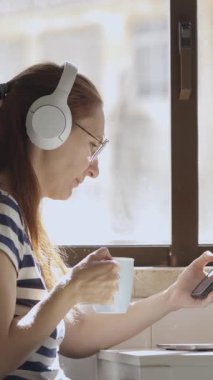 Genç bir iş kadını kahvaltı masasında cep telefonu, dizüstü bilgisayar ve kahveyle çalışıyor. Orta çekim